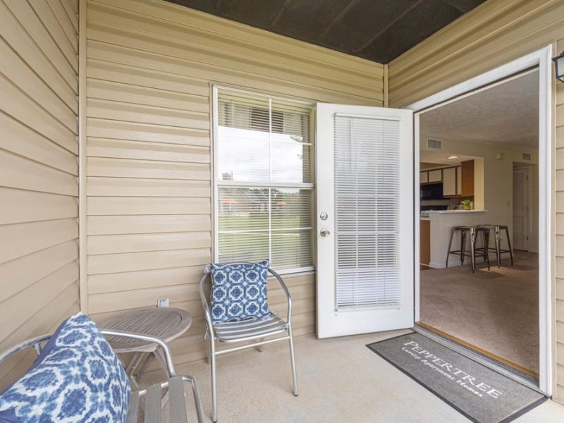 Small patio with two chairs and a table, open door leading into a kitchen and living area.