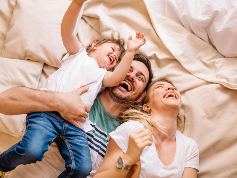 A happy family laughs together while lying on a bed, playfully enjoying each other's company.