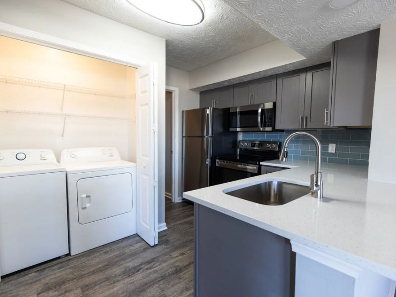 Modern kitchen with gray cabinets and stainless steel appliances next to a laundry area with washer and dryer.