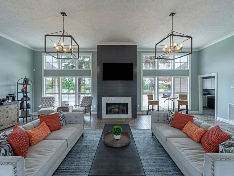 Modern living room with two sofas, a fireplace, wall-mounted TV, large windows, and decorative accents.